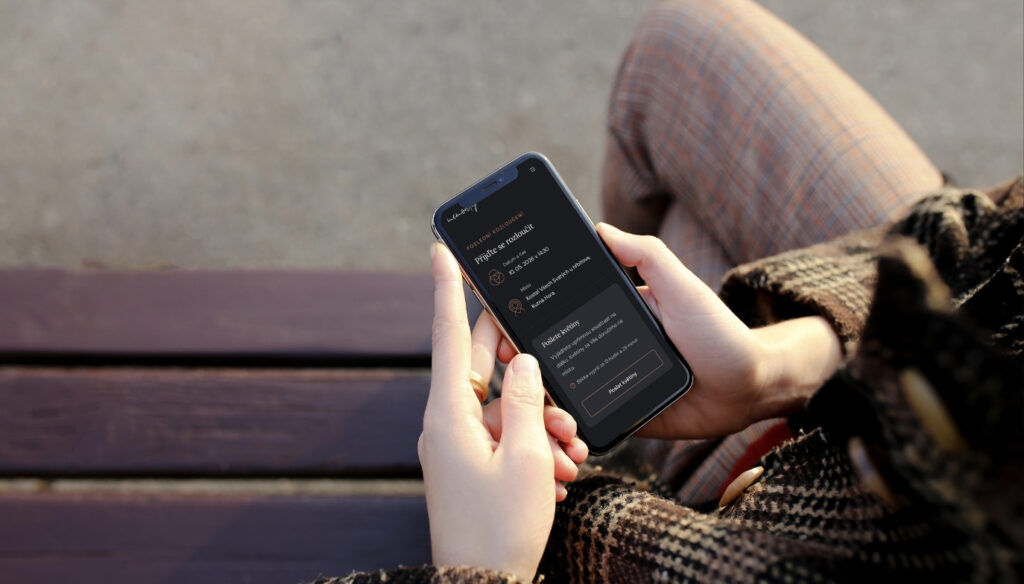 Žena sedí na lavičce a píše smuteční oznámení na mobilním telefonu.