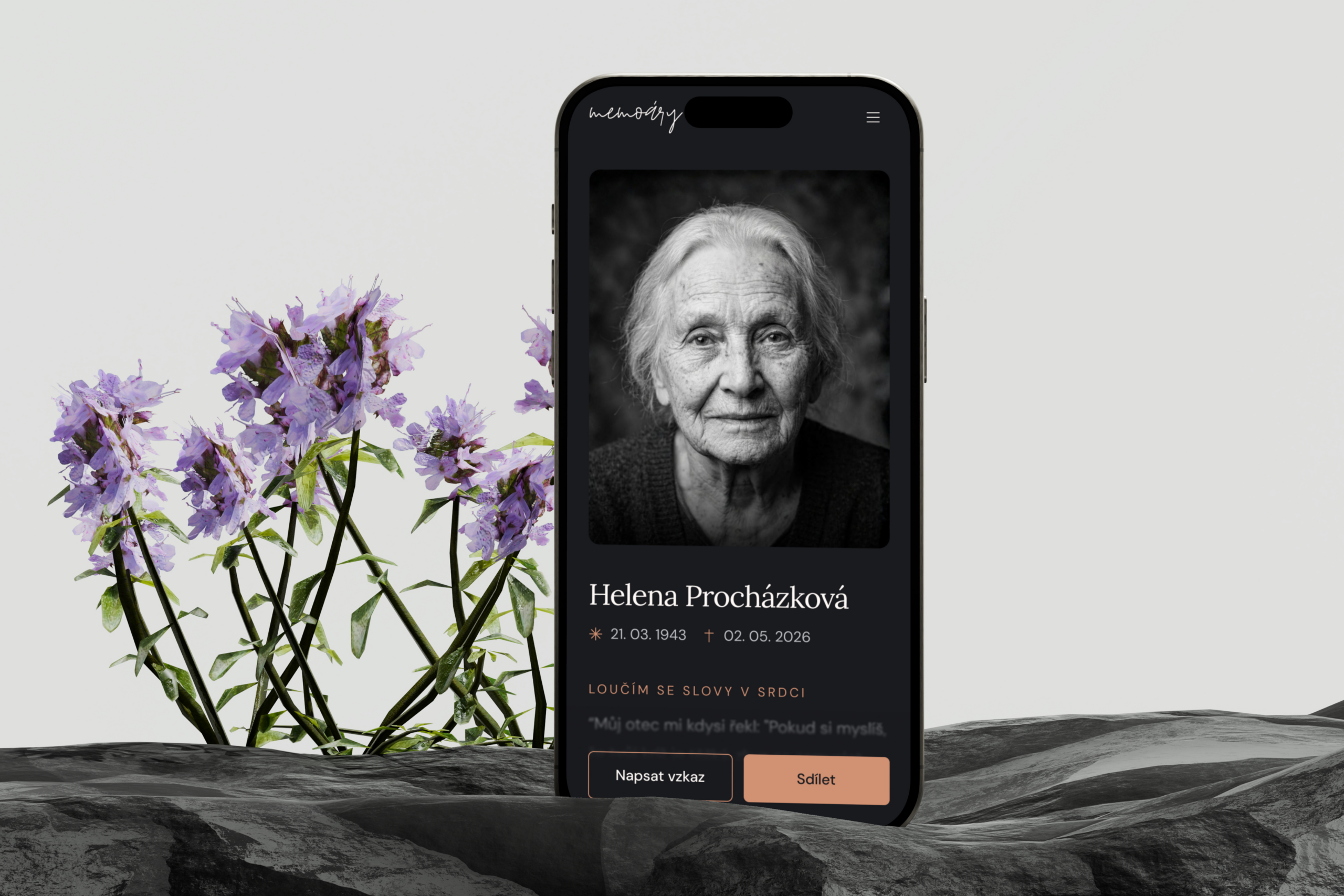 Mobilní telefon se zobrazením online vzpomínkové stránky Memoáry na tmavém kamenném podkladu s fialovými květy.