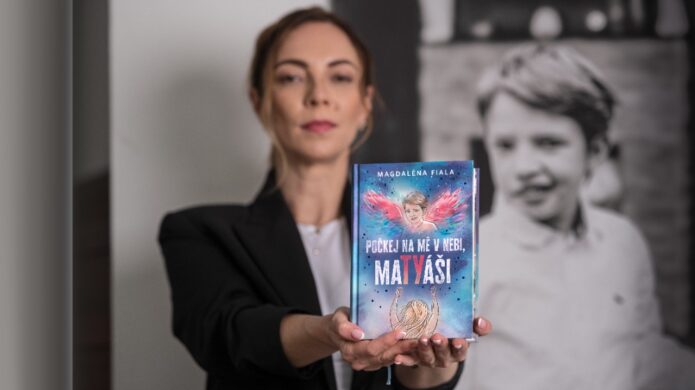 Magdaléna Fiala drží knihu Počkej na mě v nebi, MaTYáši, v pozadí je černobílá fotografie jejího syna Matyáše