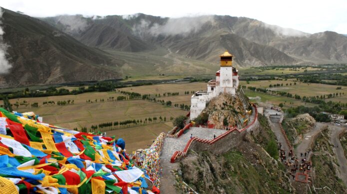 Tibetský klášter Yumbulagang na skalním výběžku s barevnými modlitebními praporky.
